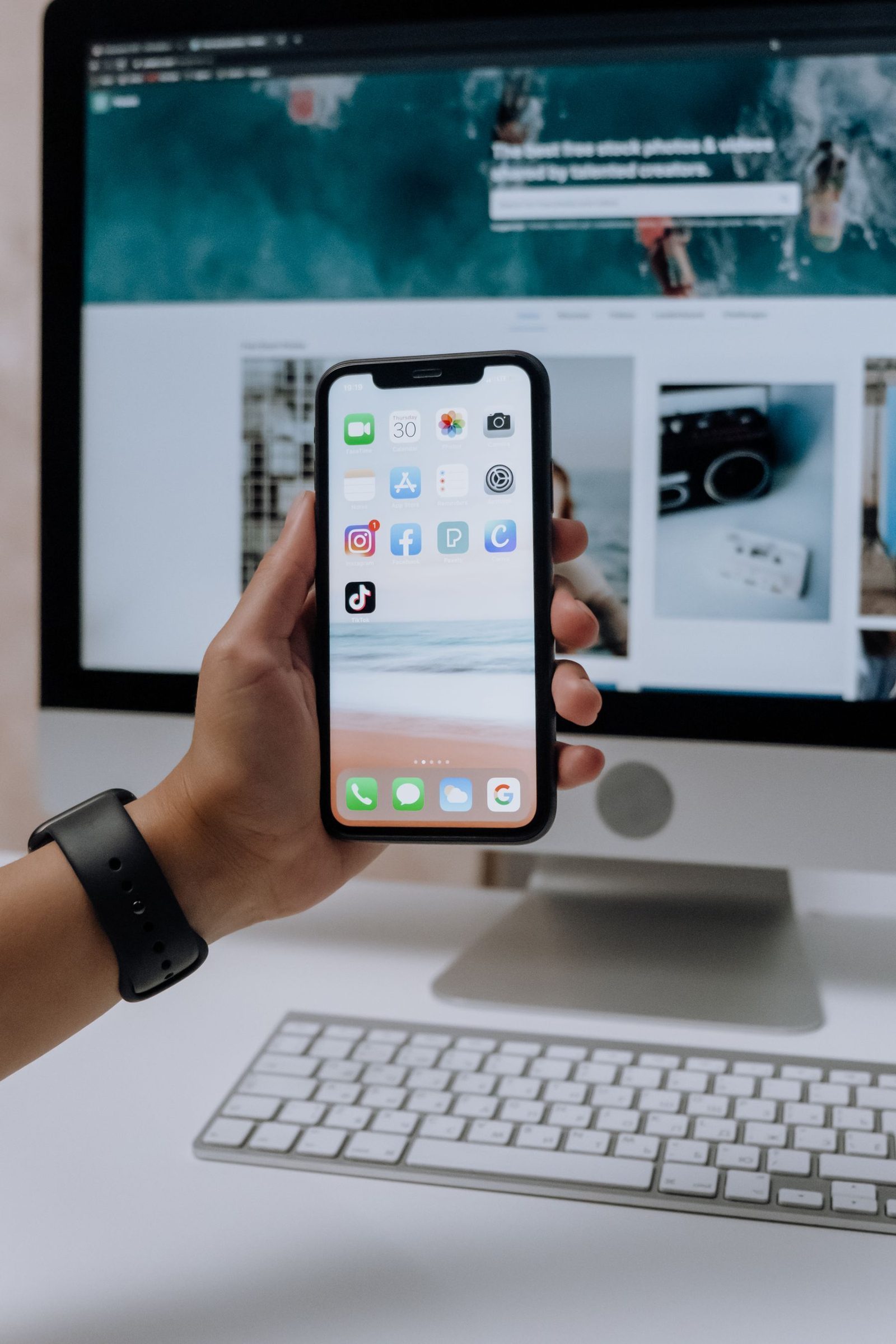 Smartphone in der Hand vor einem Bildschirm