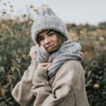 Celine in Strickmütze und hellem Mantel im herbstlichen Feld, warmes Nachmittagslicht