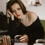 Vivienne in schwarzer Bluse an einem Cafétisch mit Kaffeetasse, gedämpftes Tageslicht