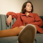 Noemi in orangefarbenem Blazer entspannt auf einem Sofa, warme Farbtöne