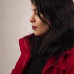 Noemi im roten Mantel im Profil, ruhiger heller Hintergrund