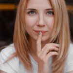 Aurelia, blonde Frau mit schulterlangem Haar, blickt ruhig in die Kamera, warmes Licht vor dunklem Hintergrund
