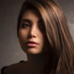 Noemi mit langem kupferrotem Haar, warmes Portrait vor dunklem Hintergrund