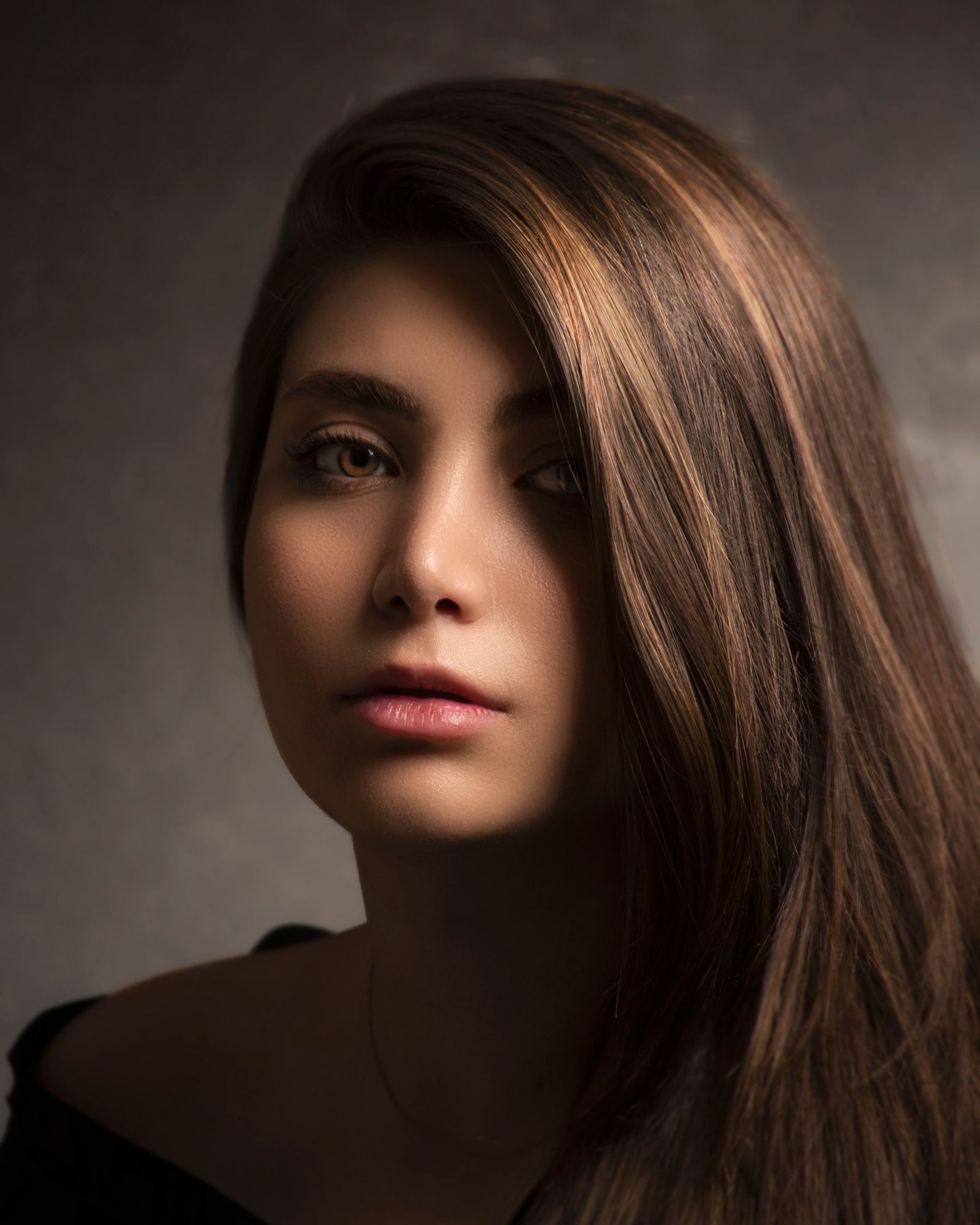 Noemi mit langem kupferrotem Haar, warmes Portrait vor dunklem Hintergrund