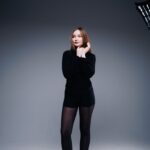 Noemi in schwarzem Rollkragenpullover vor grau-blauem Studiohintergrund, rotes Haar